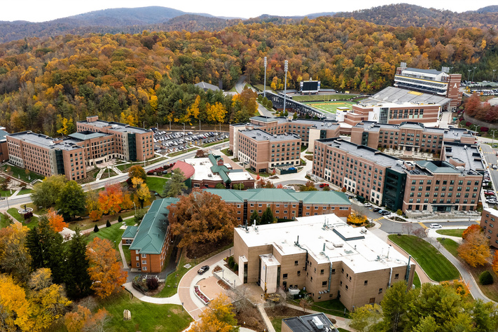 Aerial view of Appalachian State residence halls and campus buildings surrounded by colorful Blue Ridge Mountain fall foliage.