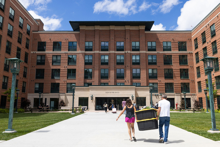 People carry belongings toward New River Hall during move-in day at a campus residence hall.
