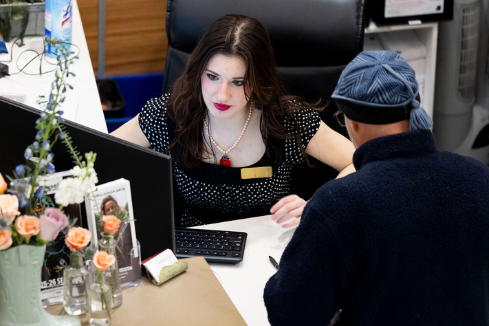 Someone receives assistance at a residence hall service desk from staff member at a computer.