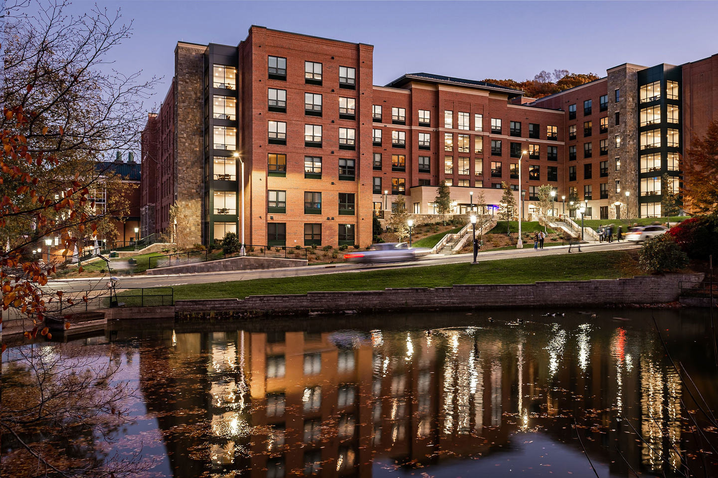 New River Residence Hall exterior at dusk reflected in a pond, showcasing modern brick architecture and landscaped grounds.