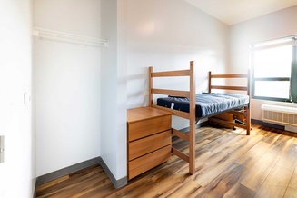 Bedroom with a raised bed, desk, dresser, wardrobe and large window.