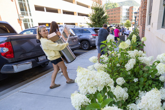 Student carries a storage bin and packed box between a vehicle and an App State residence hall.