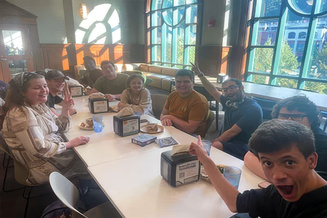 Students gather around tables in a campus dining space, sharing a meal and conversation together.