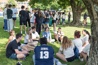 Student writes in a notebook while seated in a circle with peers during an outdoor learning activity.