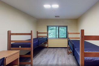 Living Learning Center standard double room with two raised beds, desks, chairs and a large window.