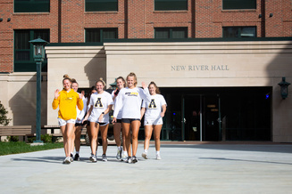 Students walk outside New River Hall residence hall on campus near the building entrance.