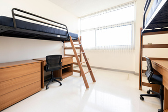 Summit Hall double room with two raised beds, desks, chairs, dressers and a large window.
