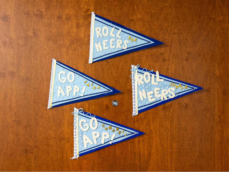 Four handmade App State pennants with student names and school spirit messages decorate a wooden door.